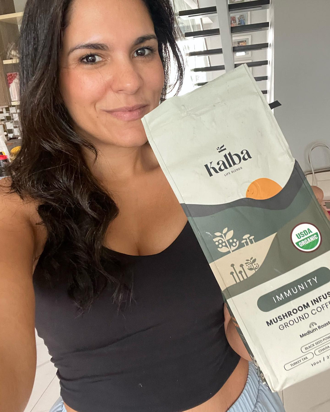 A woman holding a warm coffee at her kitchen counter in the morning